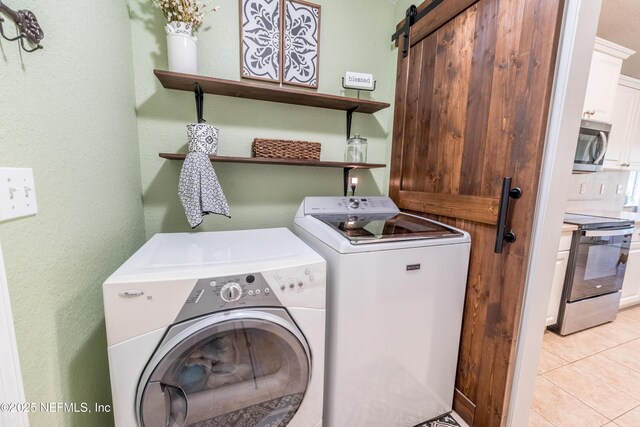 clothes washing area with light tile patterned floors, laundry area, independent washer and dryer, and a barn door