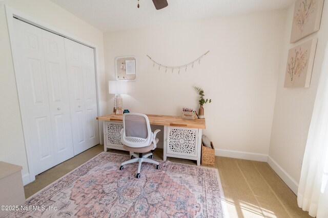 carpeted office space featuring baseboards and ceiling fan