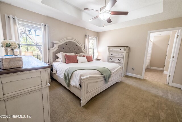 bedroom featuring a raised ceiling, multiple windows, and baseboards