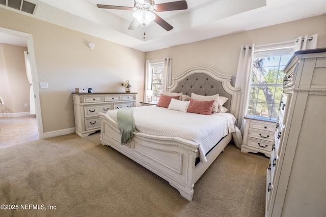 bedroom with baseboards, visible vents, ceiling fan, light carpet, and a raised ceiling