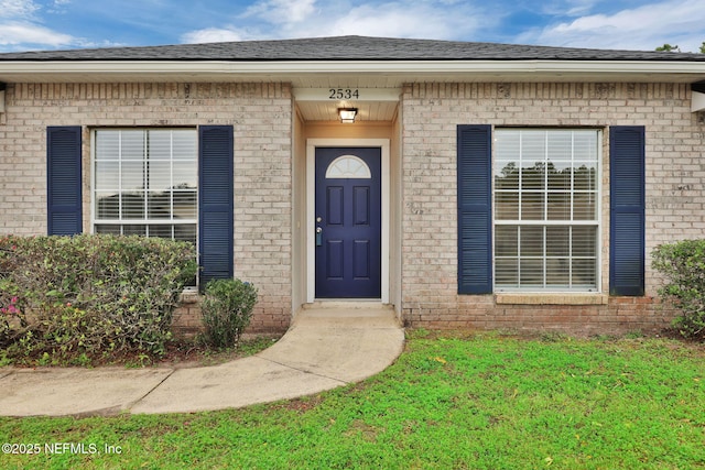 entrance to property with brick siding and a shingled roof