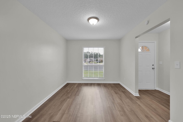 empty room with a textured ceiling, baseboards, and wood finished floors