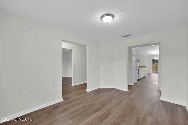 empty room featuring baseboards, visible vents, dark wood-style flooring, and a textured ceiling