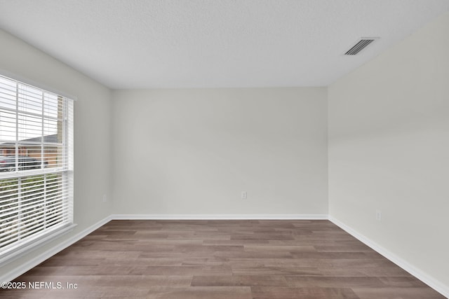 unfurnished room with visible vents, a textured ceiling, baseboards, and wood finished floors