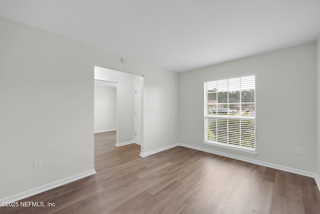 unfurnished room with baseboards, a textured ceiling, and wood finished floors