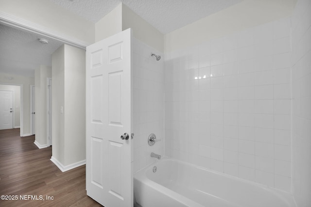 bathroom with baseboards, bathing tub / shower combination, wood finished floors, and a textured ceiling