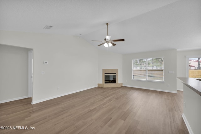 unfurnished living room featuring visible vents, lofted ceiling, wood finished floors, a glass covered fireplace, and baseboards