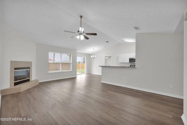 unfurnished living room with wood finished floors, visible vents, lofted ceiling, a fireplace, and ceiling fan with notable chandelier