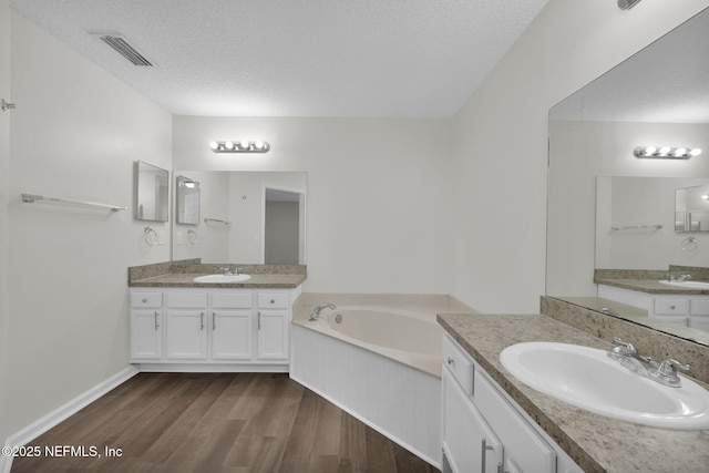 bathroom featuring a textured ceiling, wood finished floors, two vanities, and a sink