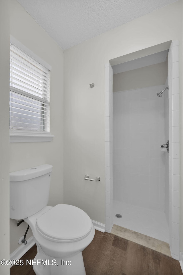 full bathroom featuring tiled shower, toilet, and a textured ceiling