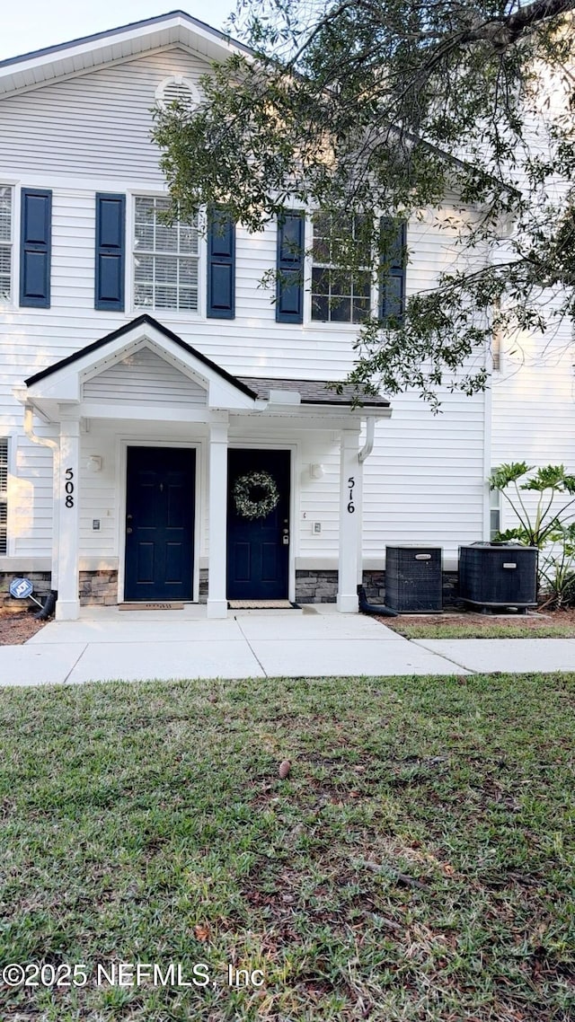 view of front facade featuring stone siding, central AC unit, and a front lawn