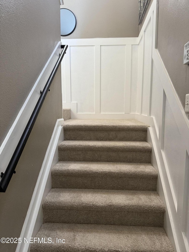 staircase featuring wainscoting and a decorative wall