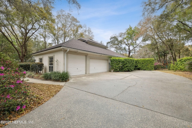 view of side of home with stucco siding, a garage, and a shingled roof