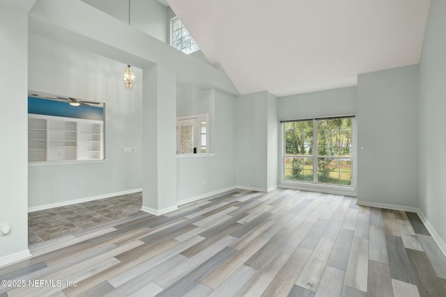 unfurnished living room with plenty of natural light, a high ceiling, baseboards, and wood finished floors