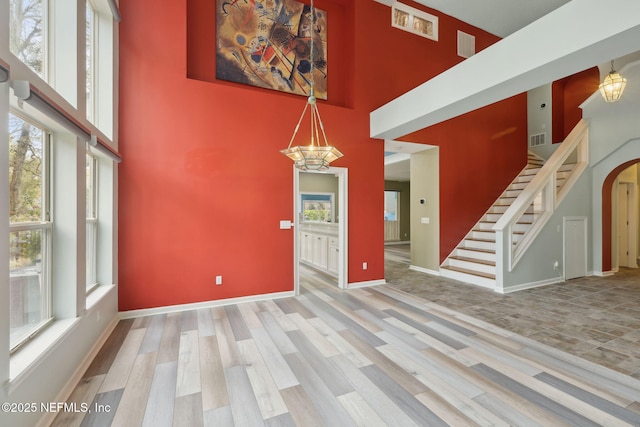 unfurnished living room featuring wood finished floors, plenty of natural light, a chandelier, and stairs