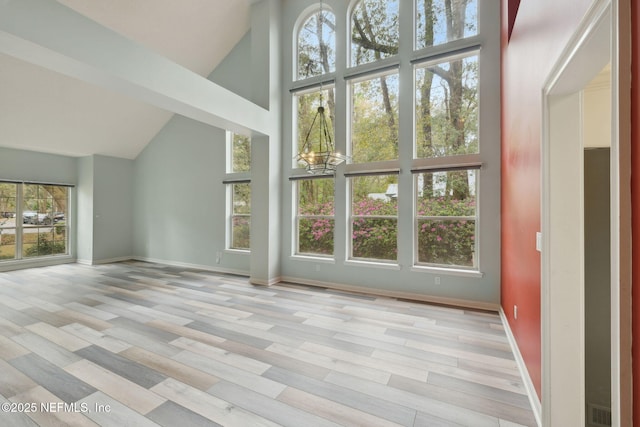 unfurnished living room featuring light wood-type flooring, baseboards, and high vaulted ceiling