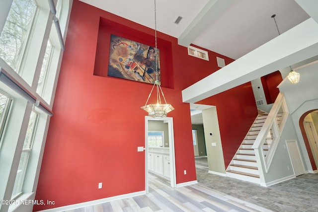 interior space featuring visible vents, wood finished floors, baseboards, a towering ceiling, and stairs