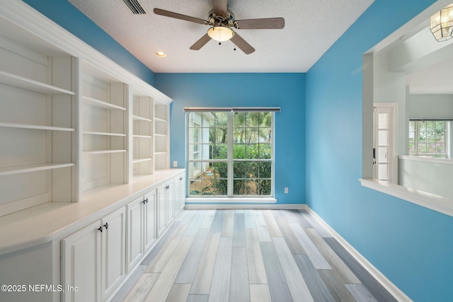 interior space with baseboards, visible vents, a textured ceiling, and light wood-style floors