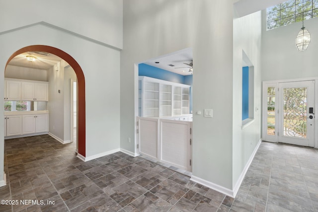 entryway featuring arched walkways, stone finish flooring, a high ceiling, and baseboards