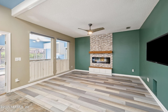 unfurnished living room with a brick fireplace, baseboards, ceiling fan, light wood-style flooring, and a textured ceiling