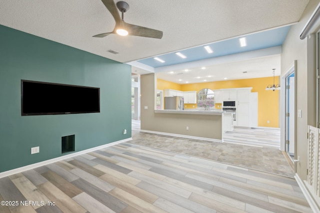 unfurnished living room featuring visible vents, ceiling fan with notable chandelier, a textured ceiling, and baseboards