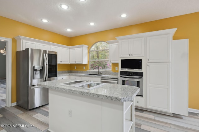 kitchen with a sink, light wood-style flooring, appliances with stainless steel finishes, and white cabinets