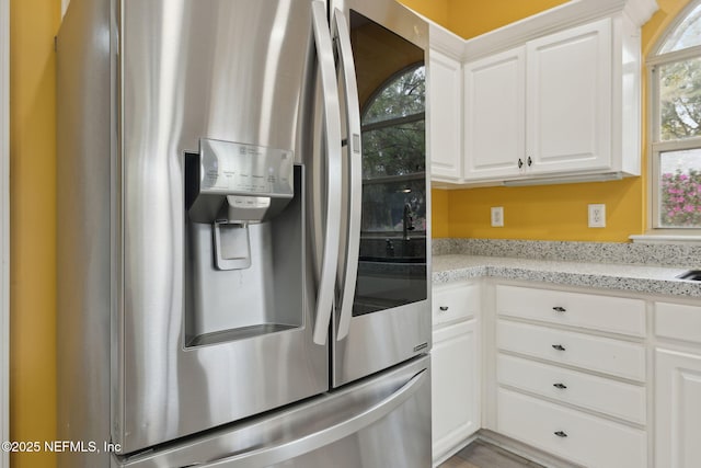 kitchen with white cabinetry, stainless steel fridge with ice dispenser, and light stone countertops