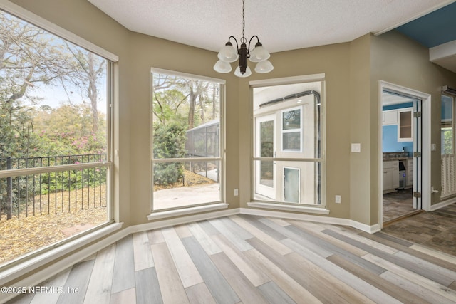 unfurnished dining area with a notable chandelier, a textured ceiling, baseboards, and wood finished floors