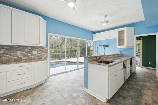 kitchen with light stone counters, a peninsula, a ceiling fan, and a sink