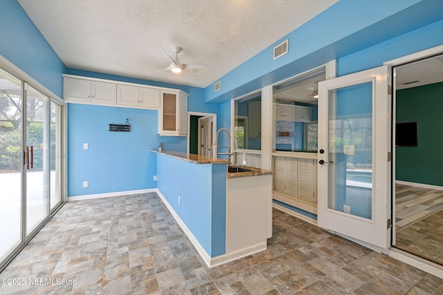 kitchen featuring visible vents, a ceiling fan, a sink, white cabinets, and glass insert cabinets