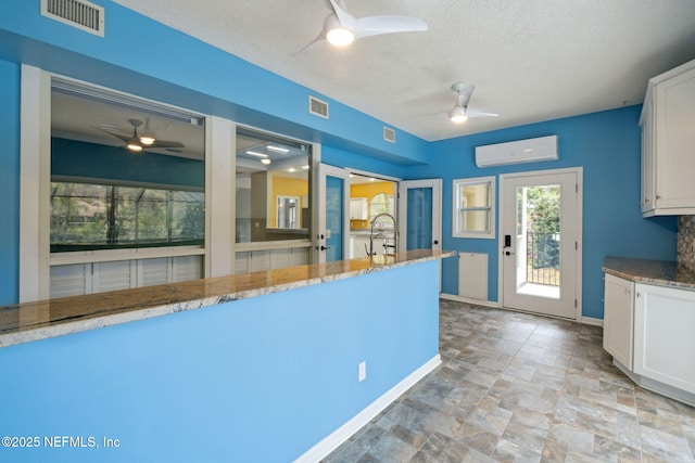 kitchen with visible vents, white cabinets, a ceiling fan, and a wall mounted AC