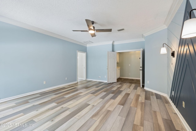 spare room with visible vents, light wood-style flooring, a textured ceiling, crown molding, and baseboards