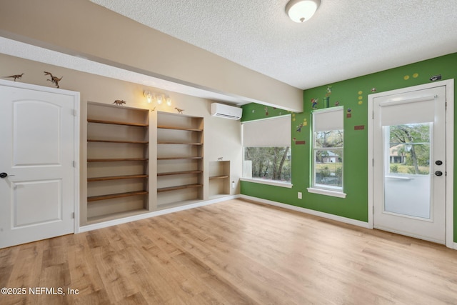 unfurnished room featuring a textured ceiling, a wall mounted AC, baseboards, and wood finished floors