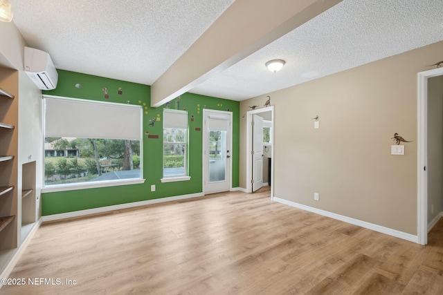 unfurnished living room featuring baseboards, a textured ceiling, a wall unit AC, and wood finished floors