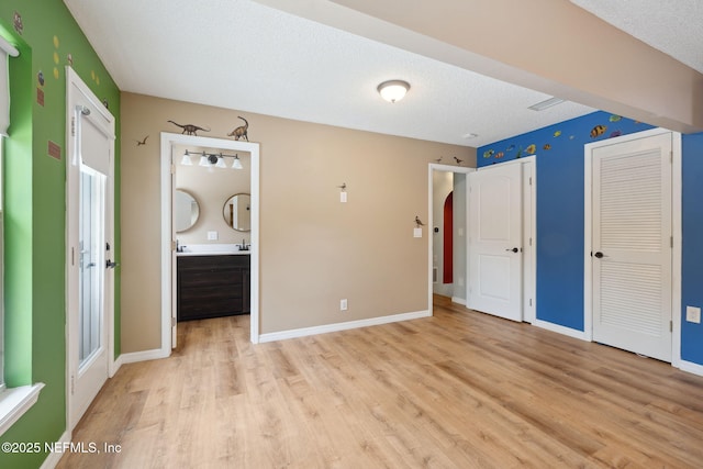 unfurnished bedroom with baseboards, a textured ceiling, light wood-type flooring, two closets, and connected bathroom