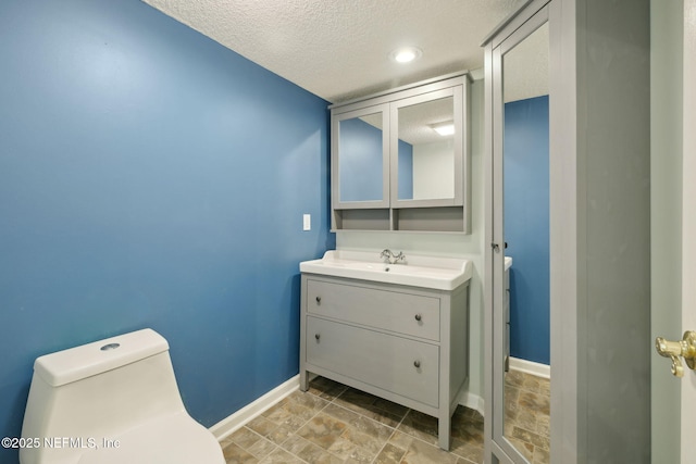 bathroom with stone finish flooring, baseboards, toilet, vanity, and a textured ceiling