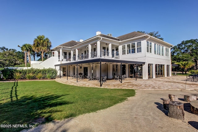 rear view of house featuring a lawn, dirt driveway, a balcony, a carport, and a patio area