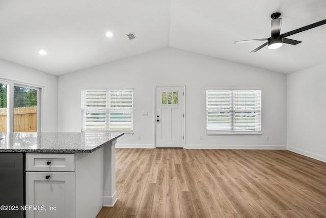 kitchen featuring light stone counters, visible vents, light wood-style flooring, and lofted ceiling