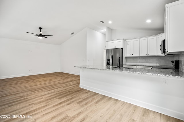 kitchen with light stone counters, light wood finished floors, stainless steel fridge with ice dispenser, electric range oven, and vaulted ceiling