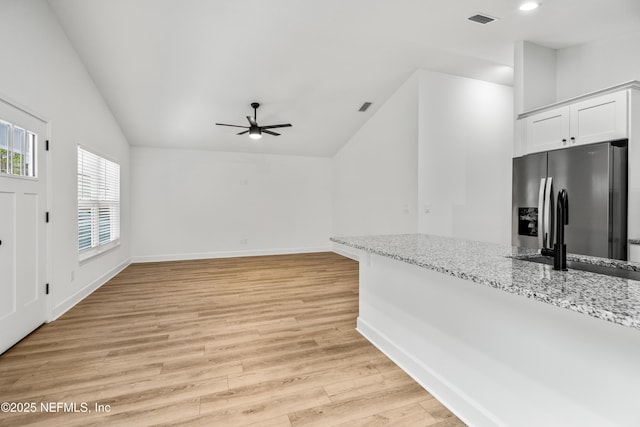 kitchen with visible vents, stainless steel fridge, light wood-style floors, lofted ceiling, and light stone countertops