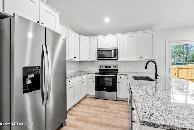 kitchen featuring a sink, backsplash, white cabinetry, stainless steel appliances, and a peninsula