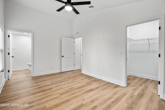 unfurnished bedroom with light wood finished floors, a spacious closet, baseboards, ensuite bath, and high vaulted ceiling