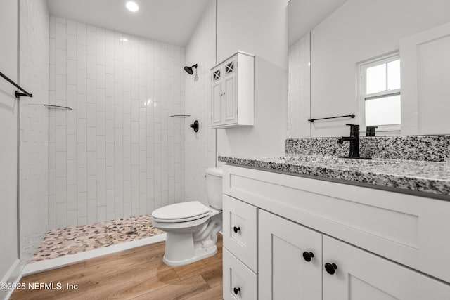 bathroom featuring toilet, a tile shower, recessed lighting, wood finished floors, and vanity