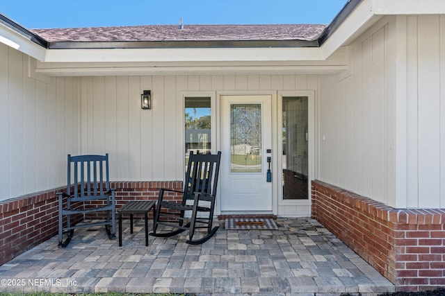 doorway to property featuring brick siding, a patio, and roof with shingles