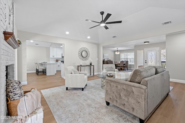 living room with light wood finished floors, visible vents, a brick fireplace, and vaulted ceiling