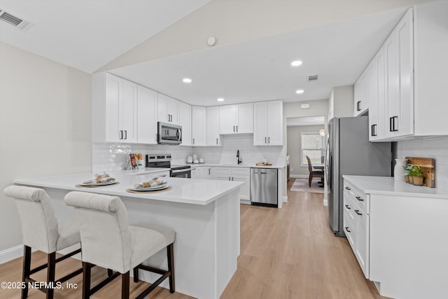 kitchen featuring visible vents, a peninsula, stainless steel appliances, a kitchen bar, and light wood-type flooring