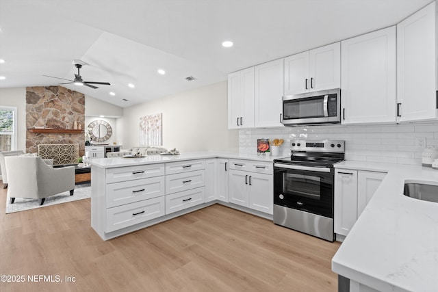 kitchen featuring appliances with stainless steel finishes, light wood-style floors, a peninsula, and vaulted ceiling