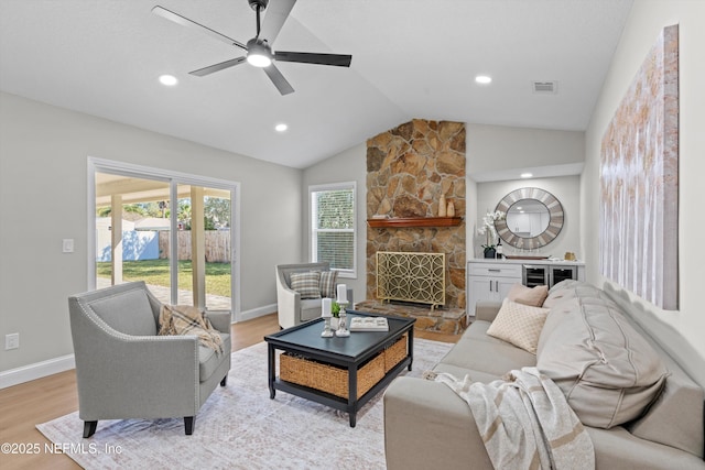 living room featuring baseboards, visible vents, lofted ceiling, a stone fireplace, and light wood-style floors