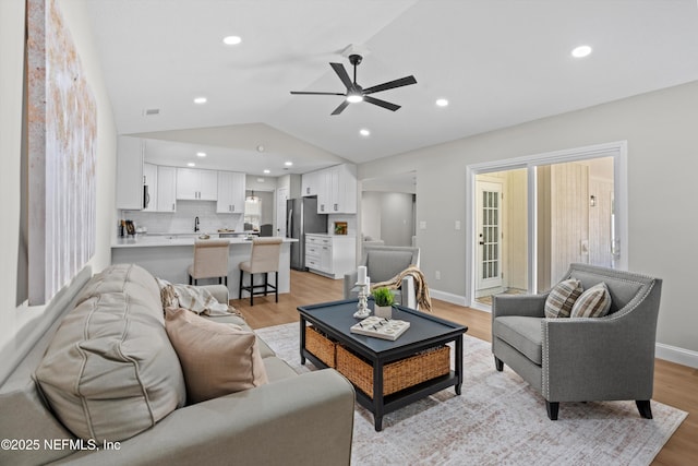 living room featuring recessed lighting, light wood-style flooring, baseboards, and vaulted ceiling