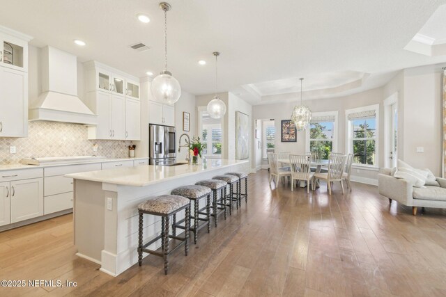 83 Village Grande Dr, Ponte Vedra, FL 32081 - kitchen featuring premium range hood, a tray ceiling, light wood-style floors, stainless steel fridge, and backsplash